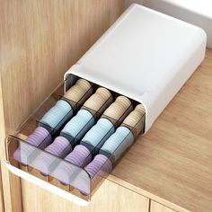 an open drawer with several different colored objects in it on a wooden countertop next to a cabinet