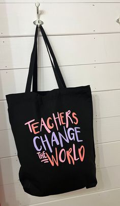 a black tote bag that says teachers change the world hanging on a white wall