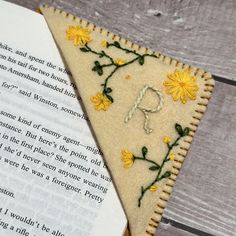 a bookmark with flowers on it next to an open book that is sitting on a wooden table