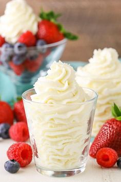 two small cups filled with whipped cream and strawberries on top of a white table