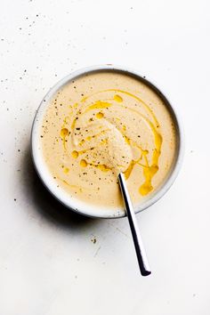 a white bowl filled with yellow liquid on top of a table next to a spoon