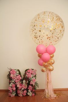 balloons and flowers are sitting on the floor next to the letter m, with one balloon in the air