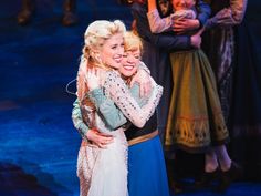 two women hugging each other on stage with people in the background and one holding her