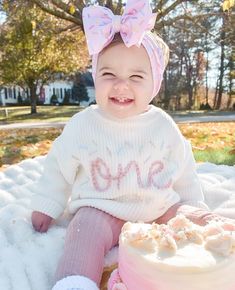 a baby sitting in the snow next to a cake with a pink bow on it