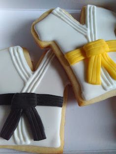 three decorated cookies in the shape of karate uniforms and black belt, on a white box