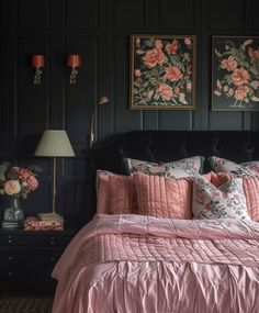 a bed with pink comforter and pillows in a dark room next to two pictures on the wall