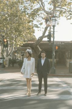 a man and woman are walking down the street in front of a tall tree with no leaves on it