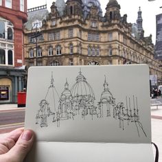 a person holding up a piece of paper with drawings on it in front of buildings