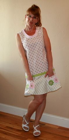 a woman standing in front of a wall wearing sandals and a dress with flowers on it