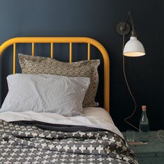 a bedroom with a yellow bed frame and black wall behind the headboard is a lamp that reads schoolhouse electric & supply co