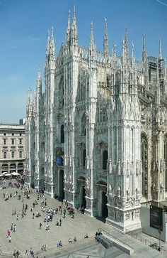 people are walking around in front of a large building with many spires and windows