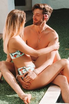 a man and woman sitting on the ground in swimsuits looking at each other