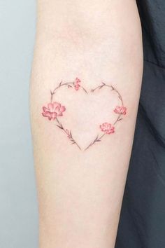 a heart shaped tattoo with pink flowers on the left side of the arm and an arrow in the middle