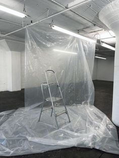 an empty white room with a ladder and plastic covering the area in front of it