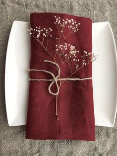 a napkin tied with twine and flowers on a white plate next to a red napkin