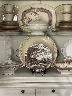 the china cabinet has many plates and dishes on it, including one with an image of a farm