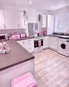 a kitchen with white cabinets and pink accessories on the counter top, along with a washer and dryer