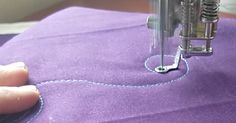 someone is stitching something on a purple piece of fabric with a sewing machine in the background