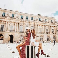 two beautiful young women sitting on top of a black and white striped pole in front of a large building