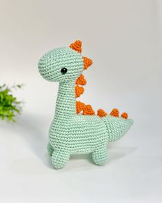 a crocheted dinosaur toy sitting next to a plant