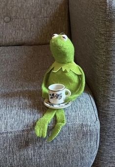 kermie the frog sitting on a couch holding a coffee cup