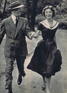 an old black and white photo of a man and woman walking down the street holding hands