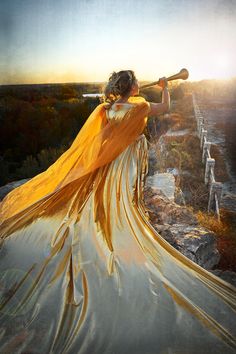 a woman in a long yellow dress holding a baseball bat on top of a hill