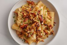 a white bowl filled with pasta covered in sauce and toppings on top of a table