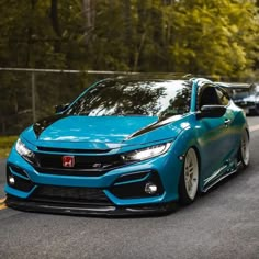 the blue car is driving down the road with other cars behind it and trees in the background