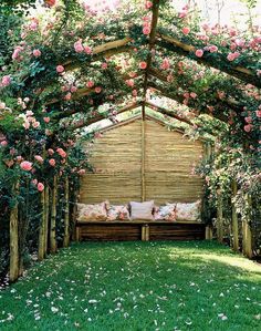 a wooden bench sitting under a pergoline covered with pink flowers and greenery