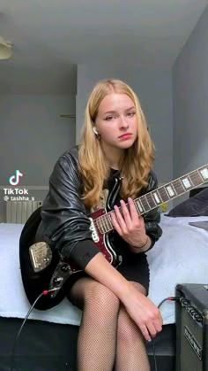 a woman sitting on top of a bed with a guitar in her hand and wearing fishnet stockings