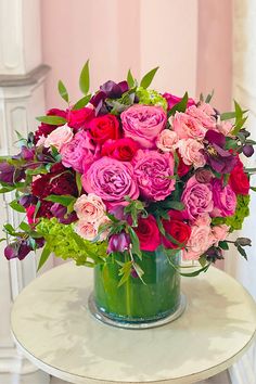 a green vase filled with lots of pink and red flowers on top of a table