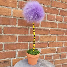 a purple pom - pom sitting on top of a potted plant next to a brick wall