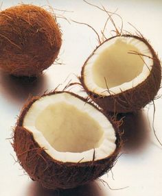 three whole coconuts with one cut open and the other half opened on a white surface