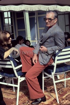 an older man sitting on top of a white chair next to a woman in red pants