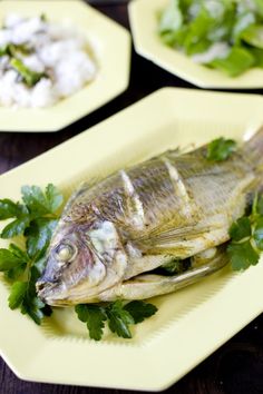 there are three plates with fish on them and garnished with parsley leaves