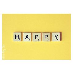 the word happy spelled with scrabble blocks on a yellow background, top view