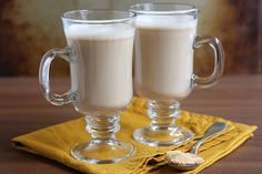 two glass mugs filled with white liquid on top of a yellow napkin