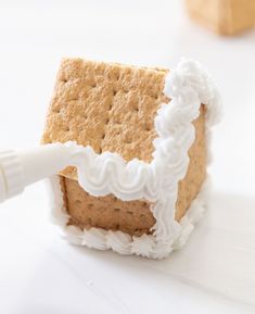 a graham cracker house with icing on it's side and a white crayon stick sticking out of the top