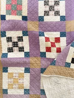 an old quilt is laying on top of a tablecloth with different colored squares in it