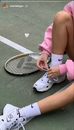 a tennis player tying her shoes on the court while sitting next to a racket