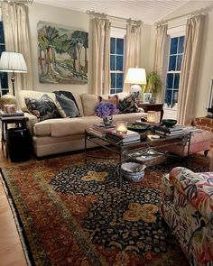 a living room filled with lots of furniture next to two windows and a rug on the floor