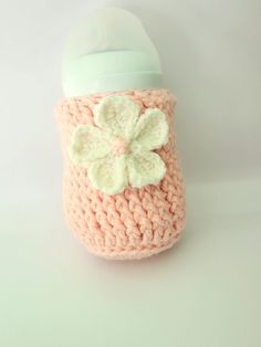 a pink crocheted cup with a white flower on the side and a green lid