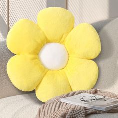 a yellow flower shaped pillow sitting on top of a couch next to a pair of glasses