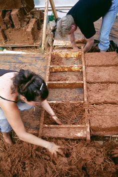 two people are working on some kind of structure in the dirt and straw, while another person is standing next to them