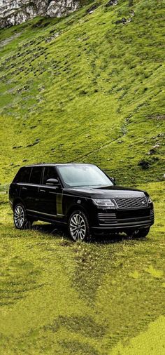 a black car parked on the side of a lush green hill next to a field