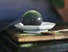 a green ball sitting on top of a white plate next to a wooden cutting board