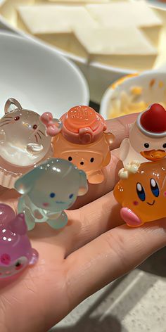 a hand holding several small plastic animals in front of some bowls with food on them