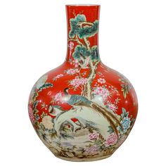 a red vase with birds and flowers painted on the side, sitting in front of a white background