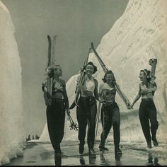 three women are holding skis and walking in the snow with ice behind them on a sunny day